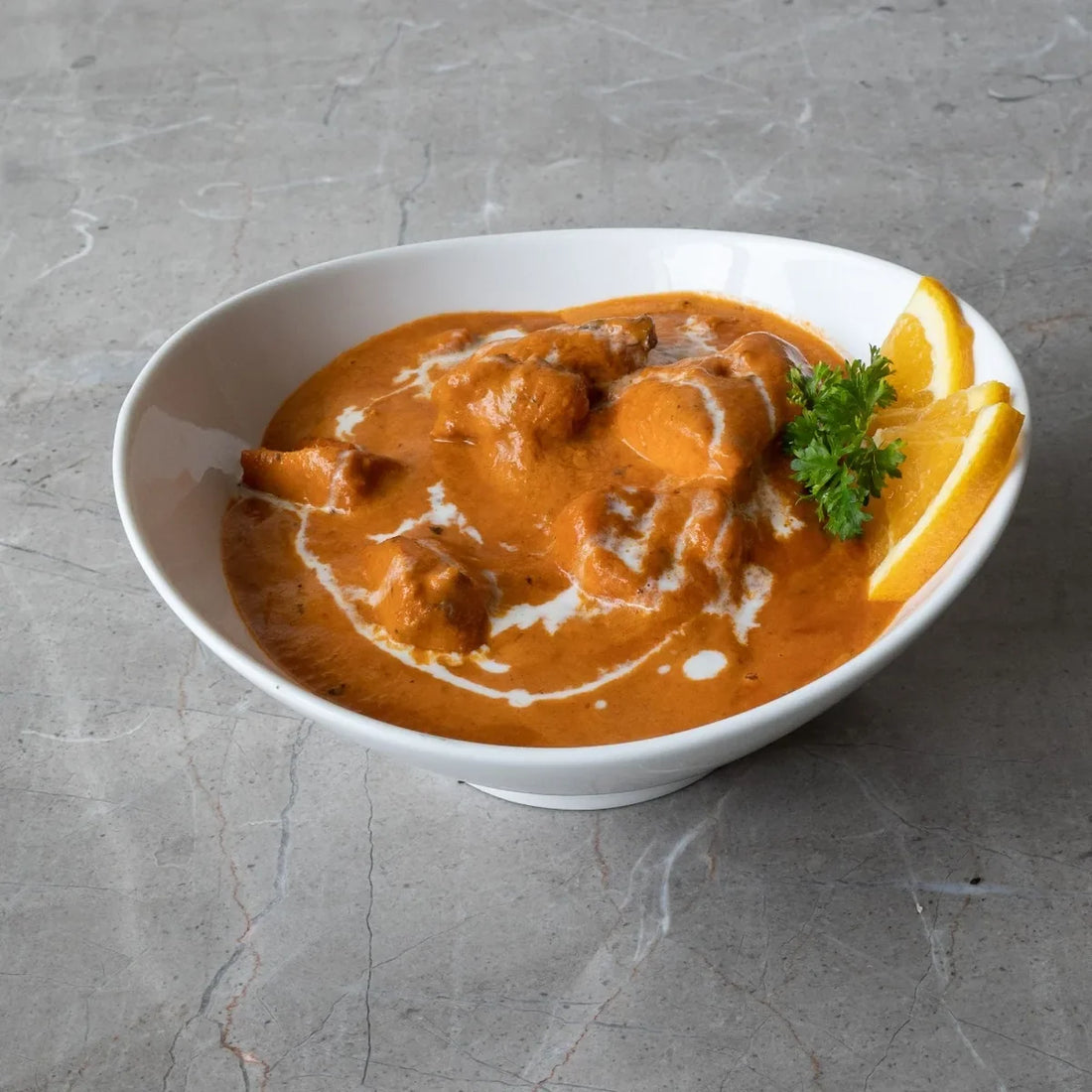 Creamy butter chicken curry with tender chicken pieces in a rich orange tomato sauce, garnished with fresh herbs.